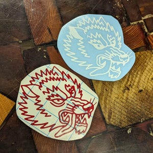 May include: Two die-cut vinyl stickers featuring wolf head designs. One is light blue with a white outline, the other is white with a red outline. Both stickers have a fierce, snarling wolf face.