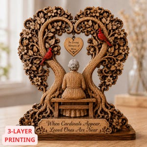 May include: A decorative wooden sculpture featuring a person sitting on a bench beneath a heart-shaped tree with two red cardinals. A heart-shaped pendant hangs from the center with the text In Loving Memory of Mom and the base reads When Cardinals Appear, Loved Ones Are Near.
