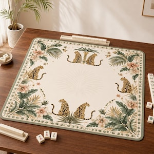 May include: A square mahjong mat featuring a cream-colored center with a repeating pattern of leopards, palm leaves, and hibiscus flowers. The border is decorated with a geometric design in shades of green, framing the central botanical illustration.