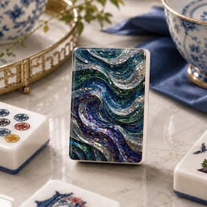 May include: A rectangular mahjong tile featuring a vibrant mosaic pattern of swirling waves in shades of deep blue, teal, purple, and iridescent silver. The tile has a smooth, glossy finish and is positioned vertically among other game pieces.
