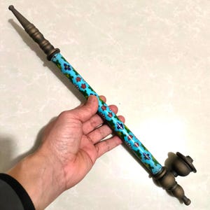 May include: An antique smoking pipe with a brass finish and a turquoise body decorated with floral patterns in red, blue, and green. The pipe has a long stem and a bowl-shaped head.
