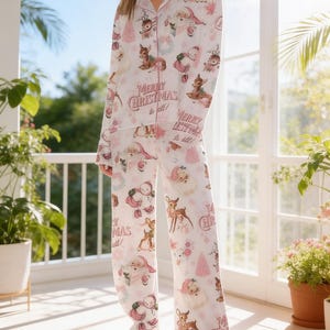 May include: White Christmas pyjama set with a festive print featuring Santa Claus, reindeer, snowmen, and Christmas trees. The set includes a button-down shirt and matching trousers, with the text "Merry Christmas to all!" in a decorative font.