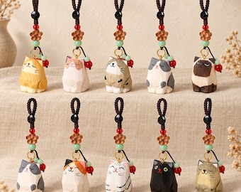 May include: Ten hand-carved wooden cat charms arranged in two rows. Each cat features a unique coat pattern and expression, suspended from a dark brown braided cord with a wooden flower bead, a small green bead, and a red bead accent.