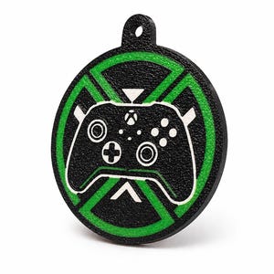Peut inclure: Un pendentif rond noir et vert avec un motif de manette Xbox. Le pendentif présente une surface texturée avec un contour vert et un graphisme de manette blanc. Il y a un petit trou en haut pour l'accrocher.