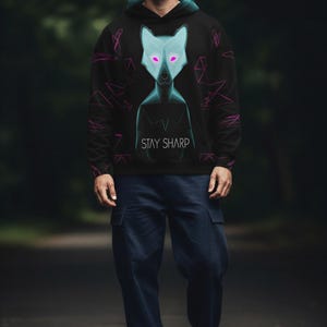 Peut inclure: Un sweat à capuche noir arborant un motif de loup géométrique bleu clair aux yeux roses lumineux et le texte STAY SHARP imprimé en blanc. Le sweat inclut une doublure de capuche bleu sarcelle et des motifs géométriques en lignes roses.