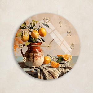 May include: A round wall clock featuring a printed still life painting of a ceramic pitcher filled with lemons and green leaves, set on a table with a striped cloth and sliced oranges. The clock face displays large, light-colored numerals 1 through 12.