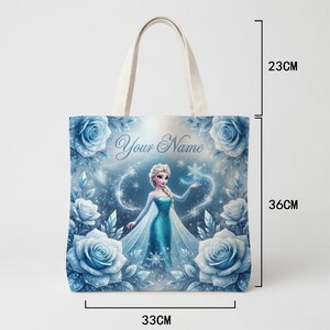 Op de afbeelding: Een canvas draagtas met een prinses in een blauwe jurk, omringd door blauwe rozen en sneeuwvlokken. De tas is 33 cm breed, 36 cm hoog en de handgreep is 23 cm. De tekst "Your Name" staat op de tas.
