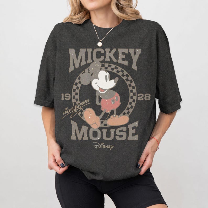 May include: Dark gray t-shirt featuring a vintage Mickey Mouse graphic. The design includes the words "Mickey Mouse" and "1928" in a distressed style, with Mickey Mouse in his classic pose. The Disney logo is at the bottom.
