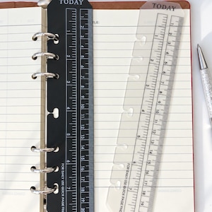 May include: Two planner page markers, one black and one translucent, each featuring the word TODAY at the top, a ruler with markings up to 8 inches and 20 cm, and the text FOR DAILY USE QUICK PAGE FINDER, positioned on a lined notebook.