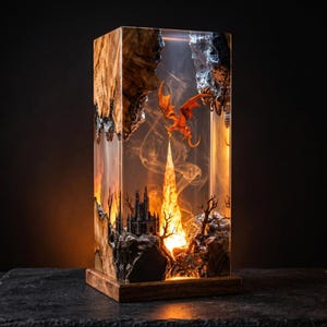 May include: A rectangular resin lamp with a fantasy scene. The lamp features a castle, a dragon, and a fiery tower. The wooden base and sides have a natural wood grain. The interior scene is illuminated with warm light.