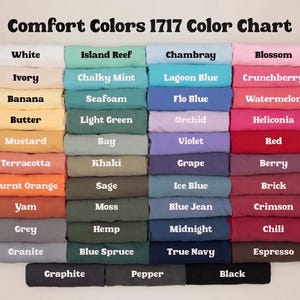 May include: A color chart titled "Comfort Colors 1717 Color Chart" displays a variety of folded fabric samples. Colors include white, ivory, banana, butter, mustard, terracotta, burnt orange, yam, grey, and granite.