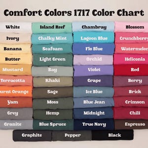 May include: A Comfort Colors 1717 color chart displaying a grid of folded fabric swatches in various shades. Each swatch is labeled with its corresponding color name, including white, ivory, banana, butter, mustard, terracotta, orange, yam, grey, granite, graphite, island reef, mint, seafoam, green, bay, khaki, sage, moss, hemp, spruce, pepper, chambray, blue, orchid, violet, grape, ice blue, navy, black, blossom, berry, red, and crimson.