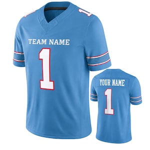 May include: A light blue sports jersey featuring the text TEAM NAME and the number 1 in white with red outlines on the front. The sleeves have red and white stripes. A second view shows the back with YOUR NAME and the number 1 in white.