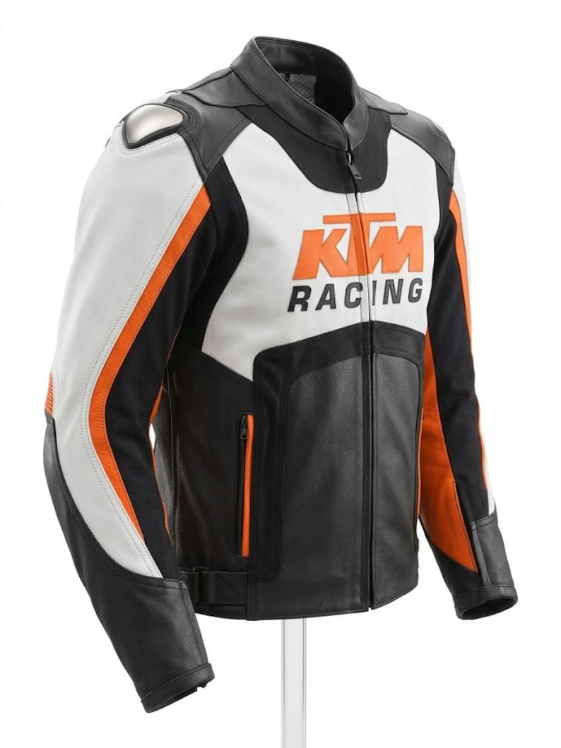 May include: A black, white, and orange motorcycle racing jacket. The jacket features the KTM Racing logo in orange on the chest. The jacket has a stand-up collar, a front zipper, and orange accents on the sleeves. The jacket has a silver shoulder protector.