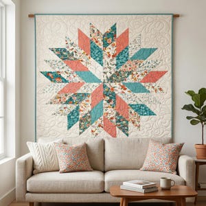 May include: A large, star-shaped quilt with a cream background and a teal border hangs on a wall. The star design features coral, teal, and floral patterned fabric. Two matching throw pillows sit on a beige sofa below the quilt.