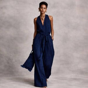 May include: A deep navy blue sleeveless jumpsuit featuring a V-neckline, a cinched waist with a matching tie belt, and wide-leg trousers. The garment has a textured fabric finish and is paired with a matching navy blue textured handbag.