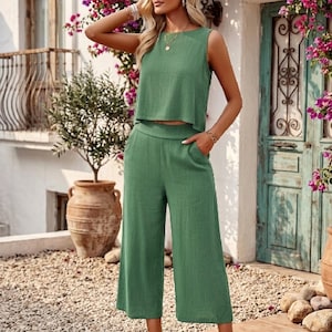 May include: A green two-piece outfit featuring a sleeveless, cropped top and wide-leg pants. The outfit is made of a textured fabric and has a casual, relaxed style. The pants have pockets. The outfit is suitable for warm weather.