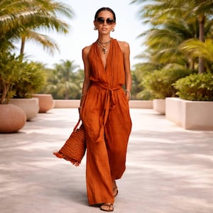 May include: A sleeveless, burnt orange jumpsuit featuring a deep V-neckline, a cinched waist with a matching tie belt, and wide-leg trousers. The garment is paired with a matching textured bucket bag and dark brown sandals.