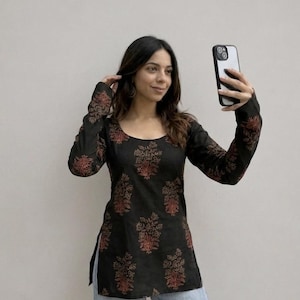 May include: Black long-sleeve tunic with a scoop neck and a floral pattern in shades of red and brown. The tunic is paired with light blue jeans. The sleeves and bodice feature the floral design.