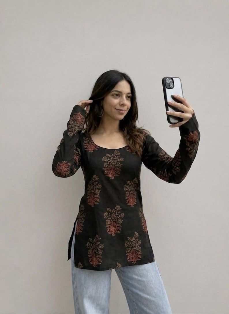 May include: Black long-sleeve tunic with a scoop neck and a floral pattern in shades of red and brown. The tunic is paired with light blue jeans. The sleeves and bodice feature the floral design.