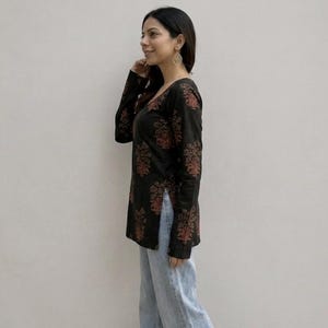 May include: Black long-sleeve top with a V-neck and a floral pattern in shades of red and orange. The top is paired with light blue jeans. The outfit is casual and suitable for everyday wear.