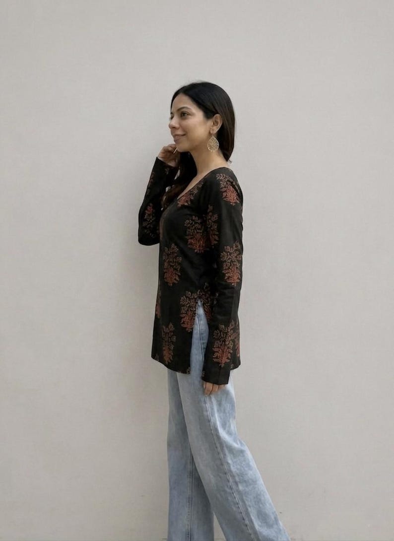 May include: Black long-sleeve top with a V-neck and a floral pattern in shades of red and orange. The top is paired with light blue jeans. The outfit is casual and suitable for everyday wear.