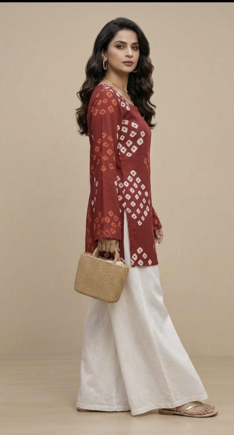 Puede incluir: Conjunto femenino que incluye una t&uacute;nica burdeos de manga larga con un estampado geom&eacute;trico blanco, combinada con pantalones blancos de pernera ancha. Un peque&ntilde;o bolso de mano tejido completa el conjunto. Adecuado para ocasiones informales o semiformales.