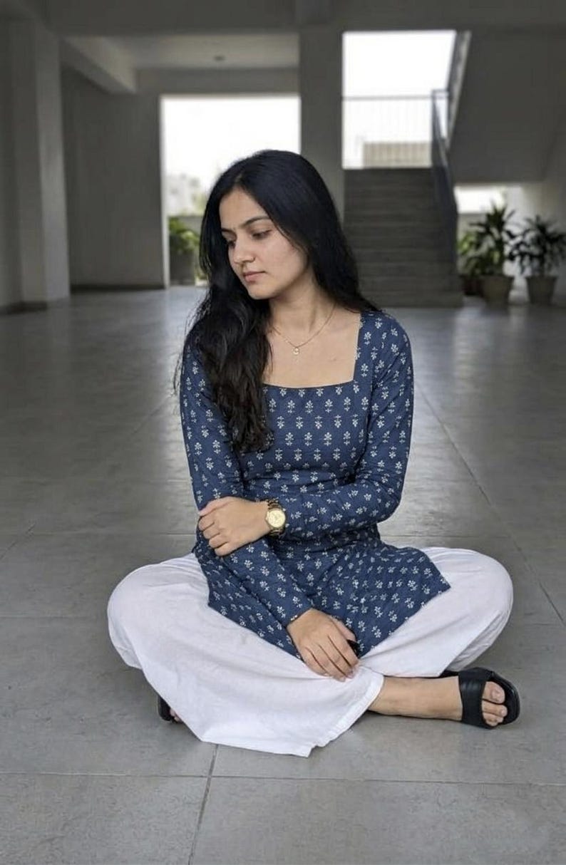 May include: A woman wearing a blue floral print long-sleeve top and white pants. The top has a square neckline and the pants are wide-legged. She is wearing a gold watch and black sandals. The outfit is casual and comfortable.