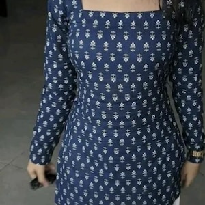 May include: A navy blue long-sleeve tunic with a square neckline and a white floral pattern. The tunic is paired with white pants. The top has a fitted silhouette and is made of a soft fabric.