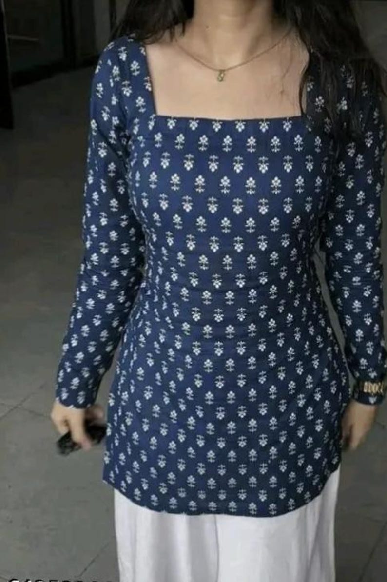 May include: A navy blue long-sleeve tunic with a square neckline and a white floral pattern. The tunic is paired with white pants. The top has a fitted silhouette and is made of a soft fabric.