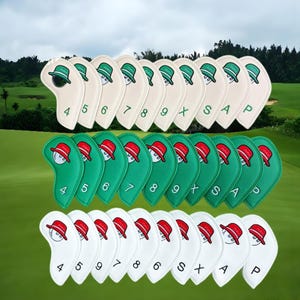 May include: A collection of golf club head covers in cream, green, and white. Each cover features an embroidered design of a golfer wearing a hat. Numbers and letters are embroidered on the covers.