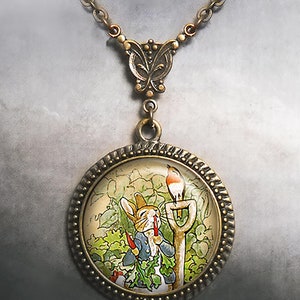 May include: A vintage-style pendant necklace with a round charm featuring a colorful illustration of a rabbit holding carrots, a bird, and a shovel. The pendant and chain are bronze-toned.