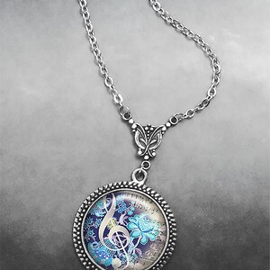 May include: A silver chain necklace with a round pendant featuring a treble clef and floral design on a vintage sheet music background. The pendant has a silver filigree butterfly charm.