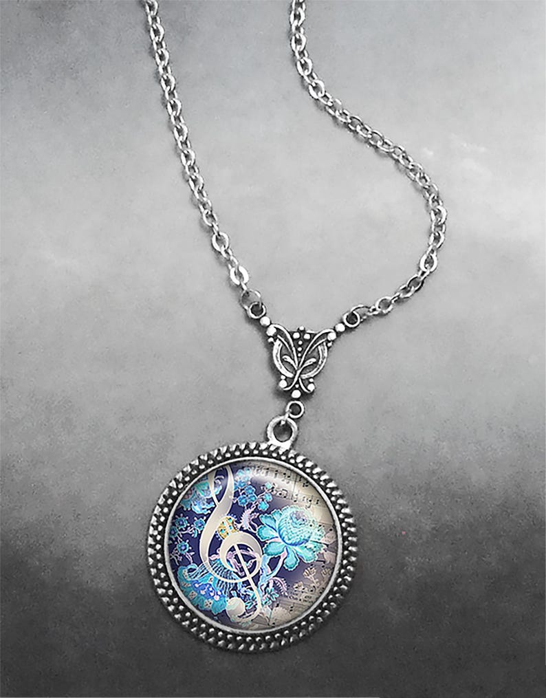 May include: A silver chain necklace with a round pendant featuring a treble clef and floral design on a vintage sheet music background. The pendant has a silver filigree butterfly charm.