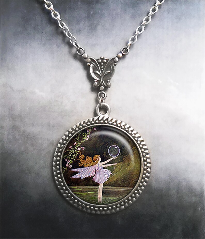 May include: Silver pendant necklace with a round charm depicting a fairy. The fairy, in a lavender dress and wings, is reaching for a bubble. The charm has a beaded edge and hangs from a delicate silver chain.