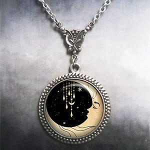 May include: A silver necklace with a round pendant featuring a crescent moon with a face and a starry night sky. The pendant has a gold-colored design of a crescent moon and stars hanging from the top.