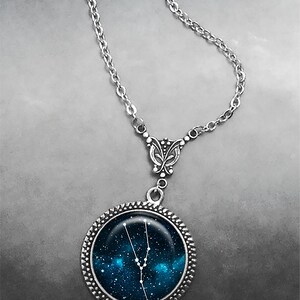 May include: A silver chain necklace with a round pendant featuring a blue galaxy background with the constellation Taurus in white.