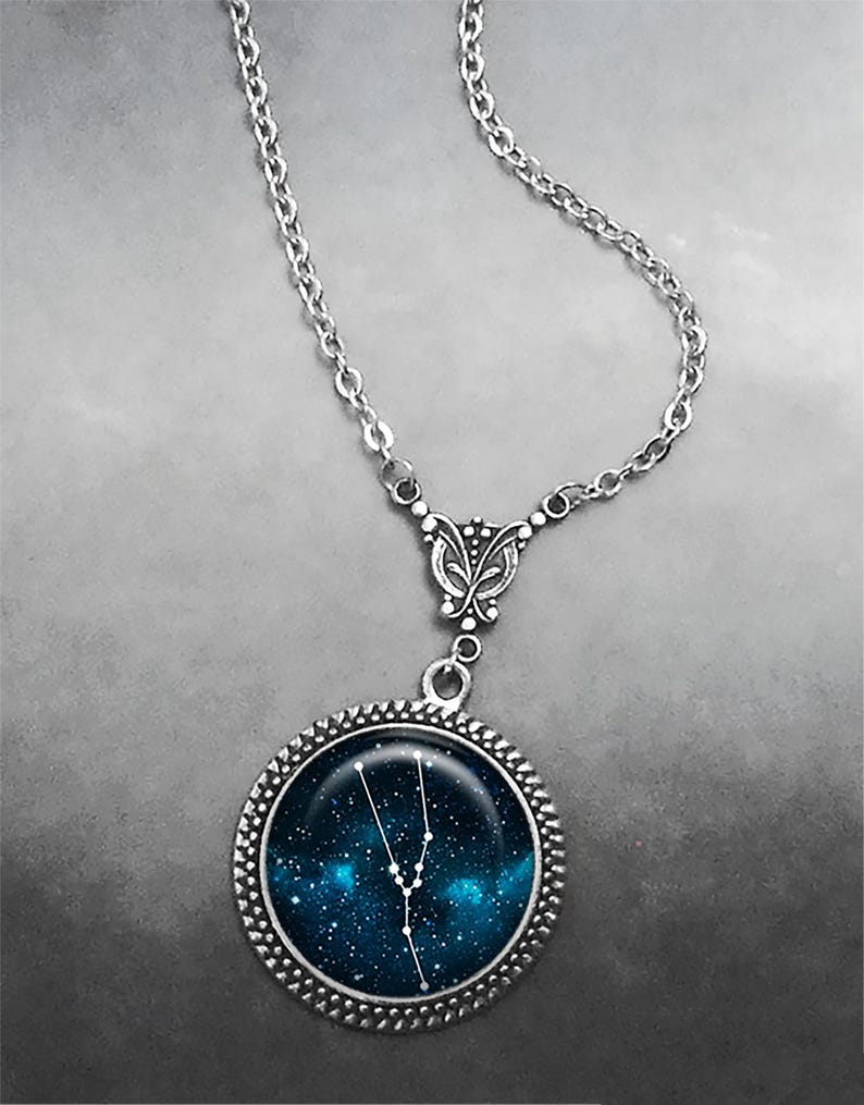 May include: A silver chain necklace with a round pendant featuring a blue galaxy background with the constellation Taurus in white.
