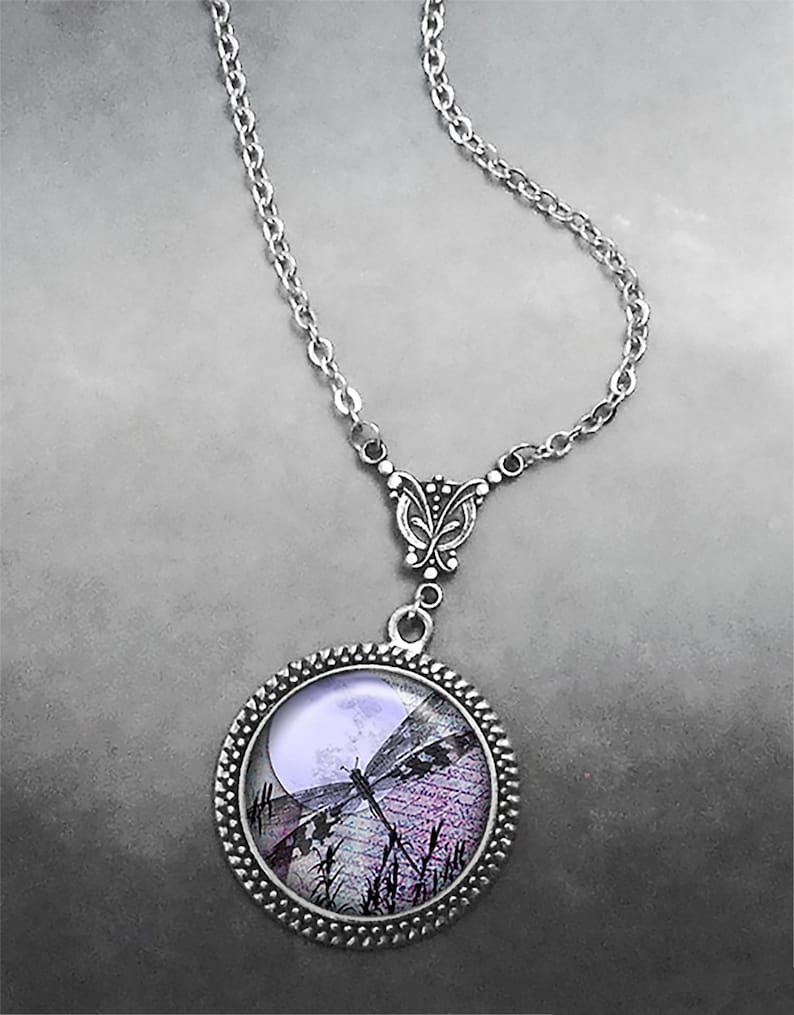 May include: Silver-toned necklace featuring a round pendant with a dragonfly design. The pendant showcases a dragonfly silhouette against a moonlit scene with purple and black hues. The chain is a delicate link style.