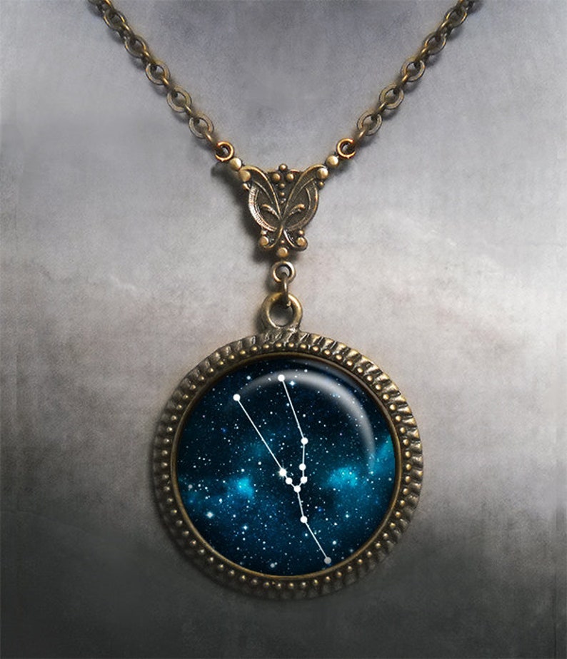 May include: A bronze necklace with a round pendant featuring a depiction of the Taurus constellation against a dark blue starry sky background.