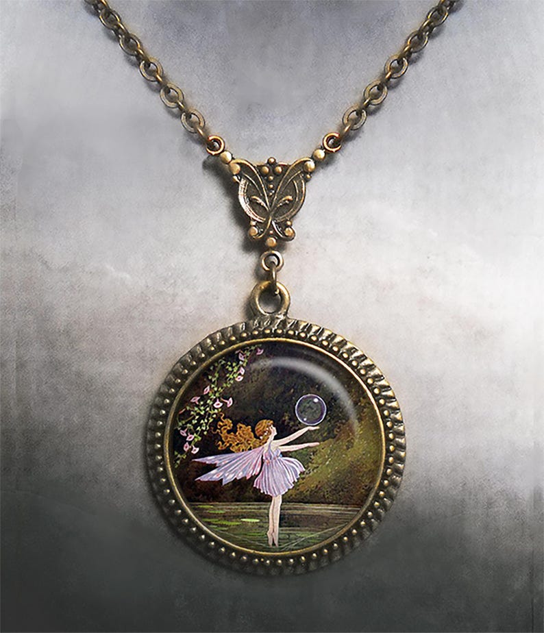 May include: A bronze-coloured necklace with a round pendant showing a fairy. The fairy is in a light purple dress, holding a bubble. The pendant has a decorative border and hangs from a chain.