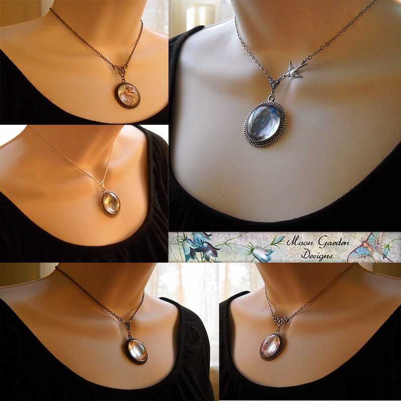 May include: Four necklaces with oval-shaped glass pendants featuring different designs. The pendants are set in silver-toned bezels and hang from silver-toned chains. The necklaces are displayed on mannequins wearing black shirts.