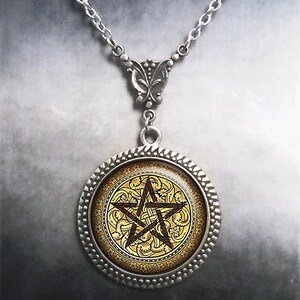May include: A silver-toned pendant necklace featuring a circular frame with a textured edge. The center displays a dark brown pentagram symbol set against a gold-colored background with an intricate, repeating floral and vine pattern.