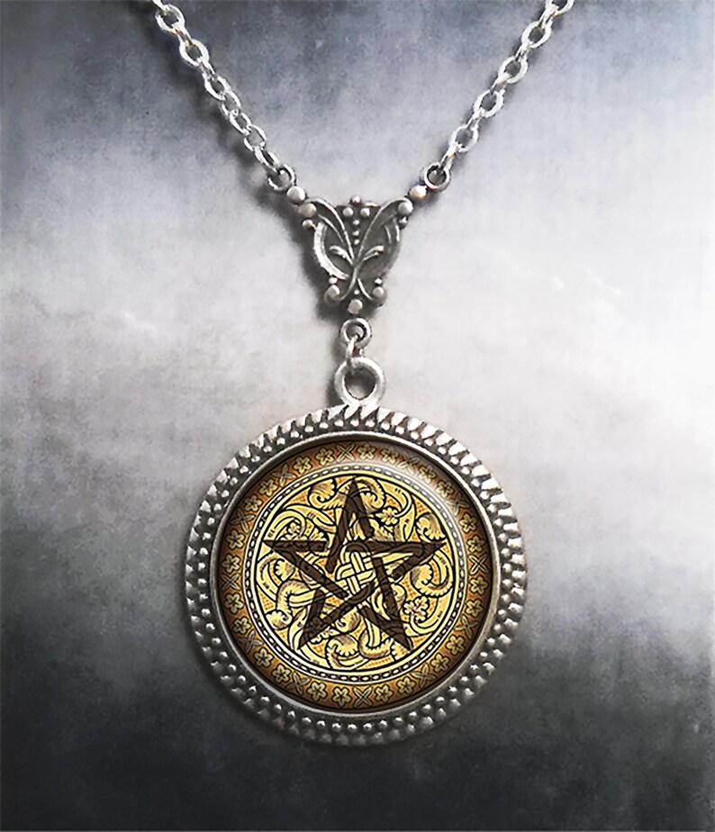 May include: A silver-toned pendant necklace featuring a circular frame with a textured edge. The center displays a dark brown pentagram symbol set against a gold-colored background with an intricate, repeating floral and vine pattern.