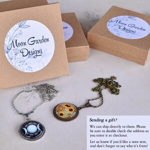 May include: Two necklaces with pendant designs, one with a celestial moon phase and the other with a floral pattern, are displayed. Three small, brown gift boxes are also visible, each with a white label reading "Moon Garden Designs".