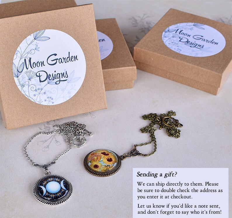 May include: Two necklaces with pendant designs, one with a celestial moon phase and the other with a floral pattern, are displayed. Three small, brown gift boxes are also visible, each with a white label reading "Moon Garden Designs".
