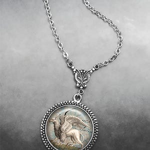 May include: A silver chain necklace with a round pendant featuring a detailed image of a griffin, a mythical creature with the head and wings of an eagle and the body of a lion.
