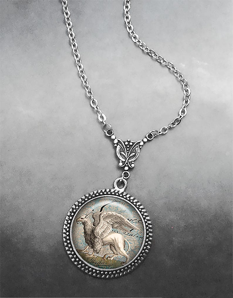 May include: A silver chain necklace with a round pendant featuring a detailed image of a griffin, a mythical creature with the head and wings of an eagle and the body of a lion.