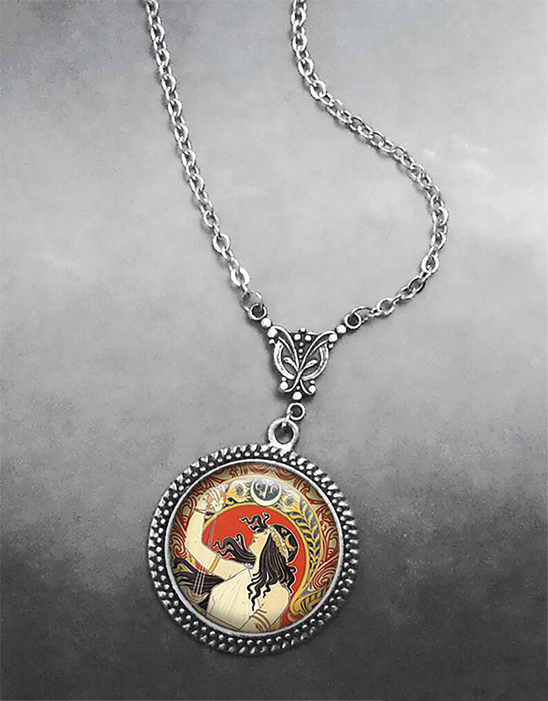 May include: A silver chain necklace with a round pendant featuring a vintage art nouveau illustration of a woman with long dark hair holding a lyre. The pendant has a silver border with a decorative pattern.