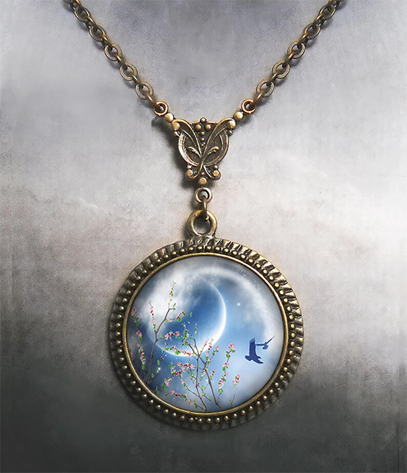 May include: A bronze necklace with a round pendant featuring a crescent moon, a branch of pink blossoms, and a blue bird flying against a blue sky.